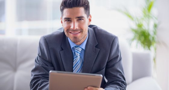 Businessman sitting on sofa using his tablet smiling at camera i